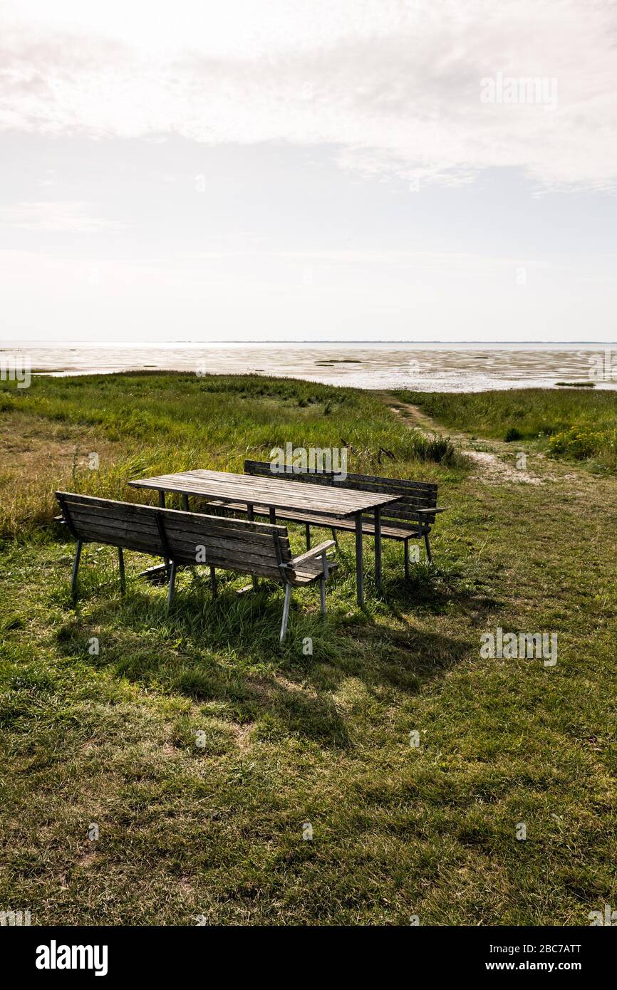 Picknicktisch mit zwei Holzbänken auf einer grünen Wiese mit Blick auf das Wattenmeer in der Sonne. Stockfoto