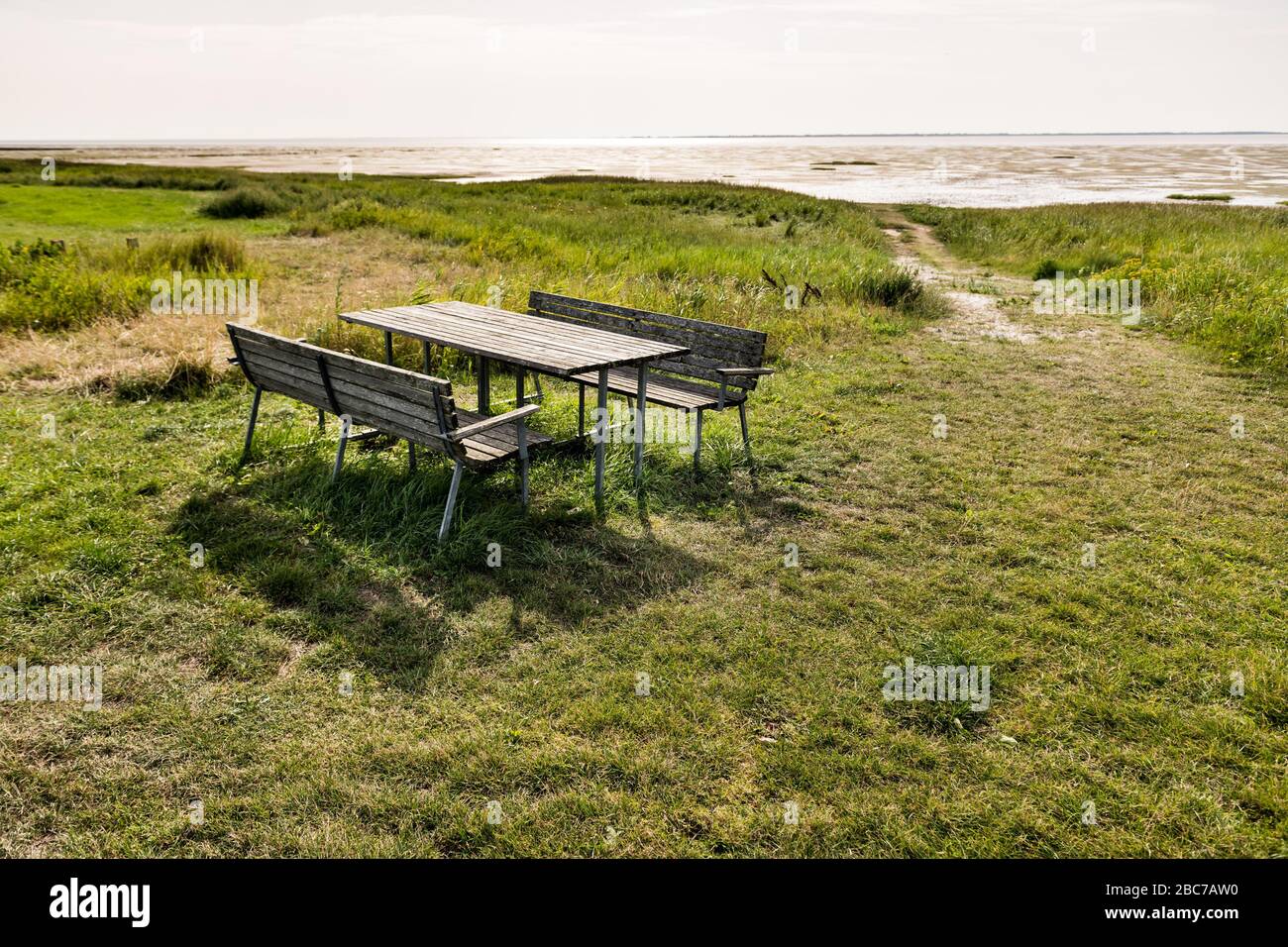 Picknicktisch mit zwei Holzbänken auf einer grünen Wiese mit Blick auf das Wattenmeer in der Sonne. Stockfoto