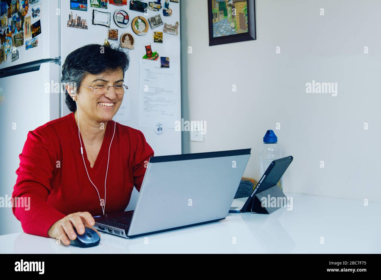 Erfolgreiche Geschäftsfrau mittleren Alters arbeitet an Quarantänetagen zu Hause in ihrer Küche. Stockfoto