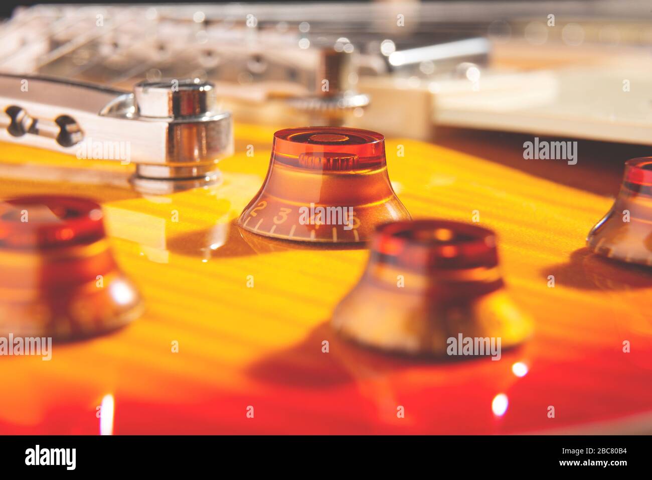 Selektive Fokussierung auf den Bernsteinknopf auf der Oberseite einer geflammten, kirschfarbenen E-Gitarre Stockfoto