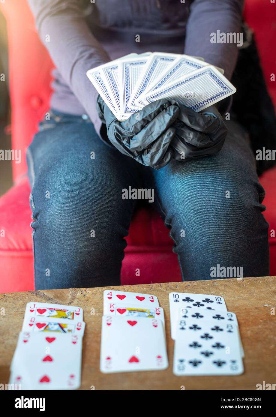 Junge Frau, die allein zu Hause Karten spielt, trägt medizinische Handschuhe, Solitare, Geduld. Stockfoto