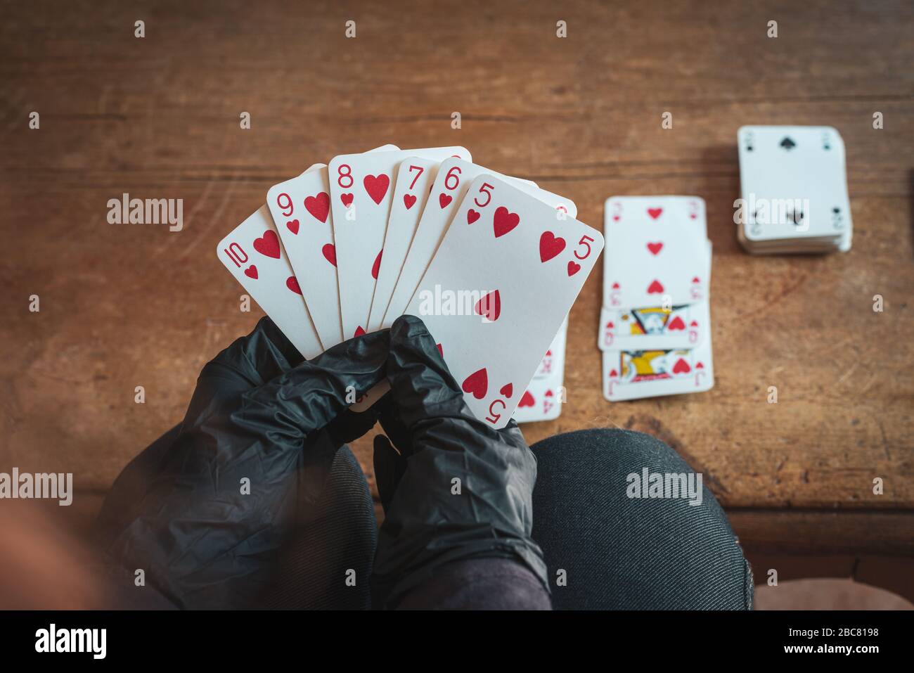 Junge Frau, die allein zu Hause Karten spielt, trägt medizinische Handschuhe, Solitare, Geduld. Stockfoto