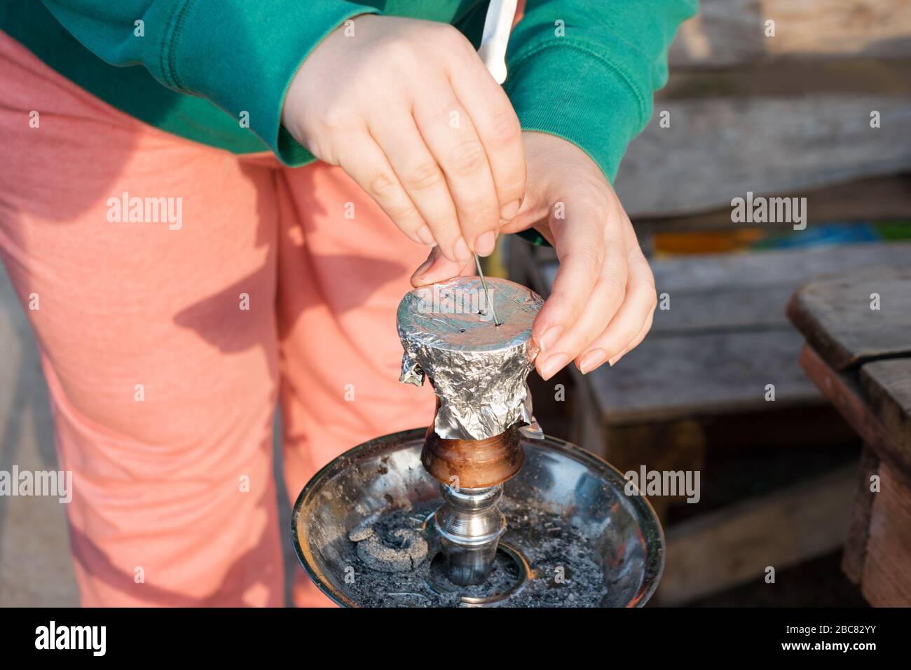 Weibliche Hand mit Hookah auf verschwommenem Hintergrund. Tasse für Hookah mit Folie gestreckt, Hände vorbereiten Hookah, Löcher in Folie machen Stockfoto