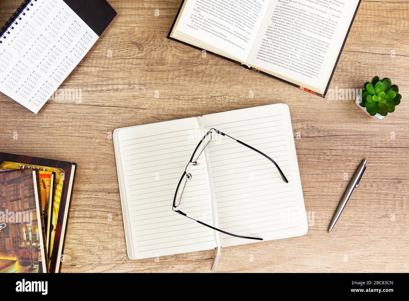 Arbeitsplatz zurück zur Schule und zum Bildungskonzept auf einem alten Holztisch mit leerem Notizblock und Stapel von Buch, Glas, Bleistift, grüner Pflanze und PAP Stockfoto