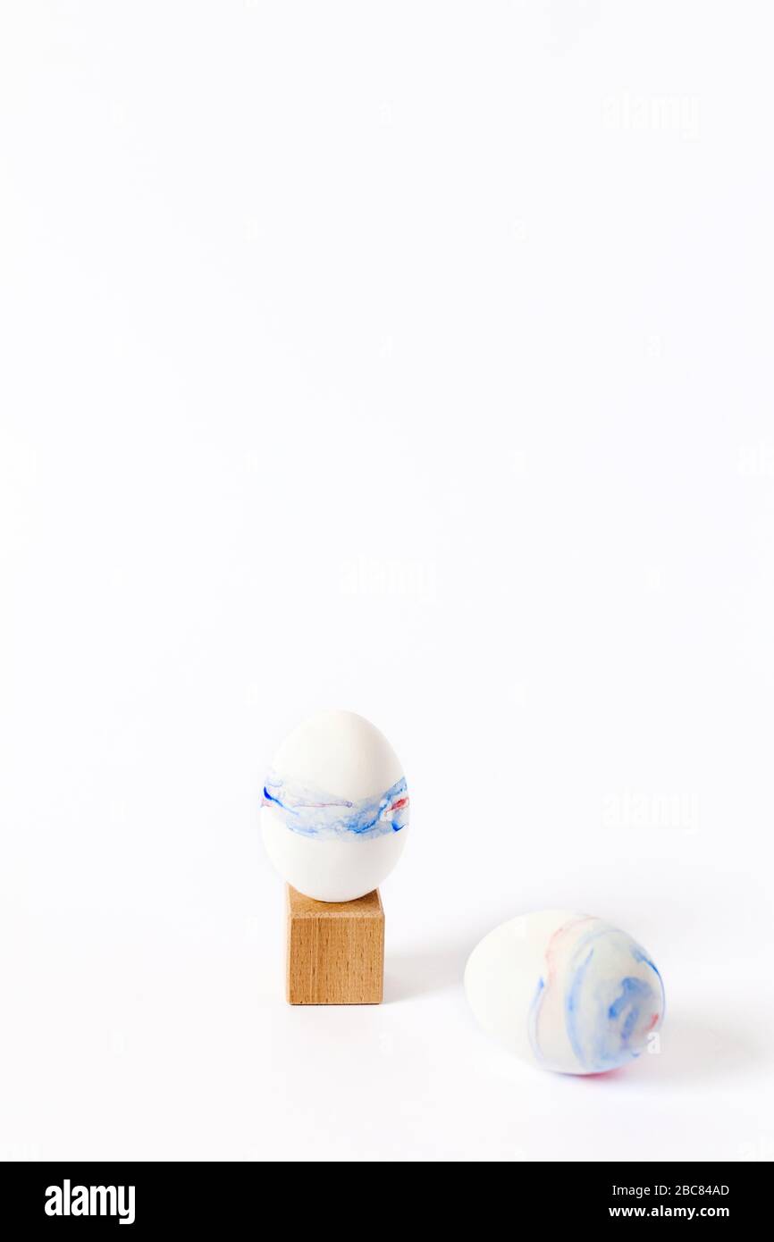 Vertikales Osterbild. Zwei mit Aquarell bemalte Eier auf einem Holzwürfel und auf einem weißen Tisch. Stockfoto