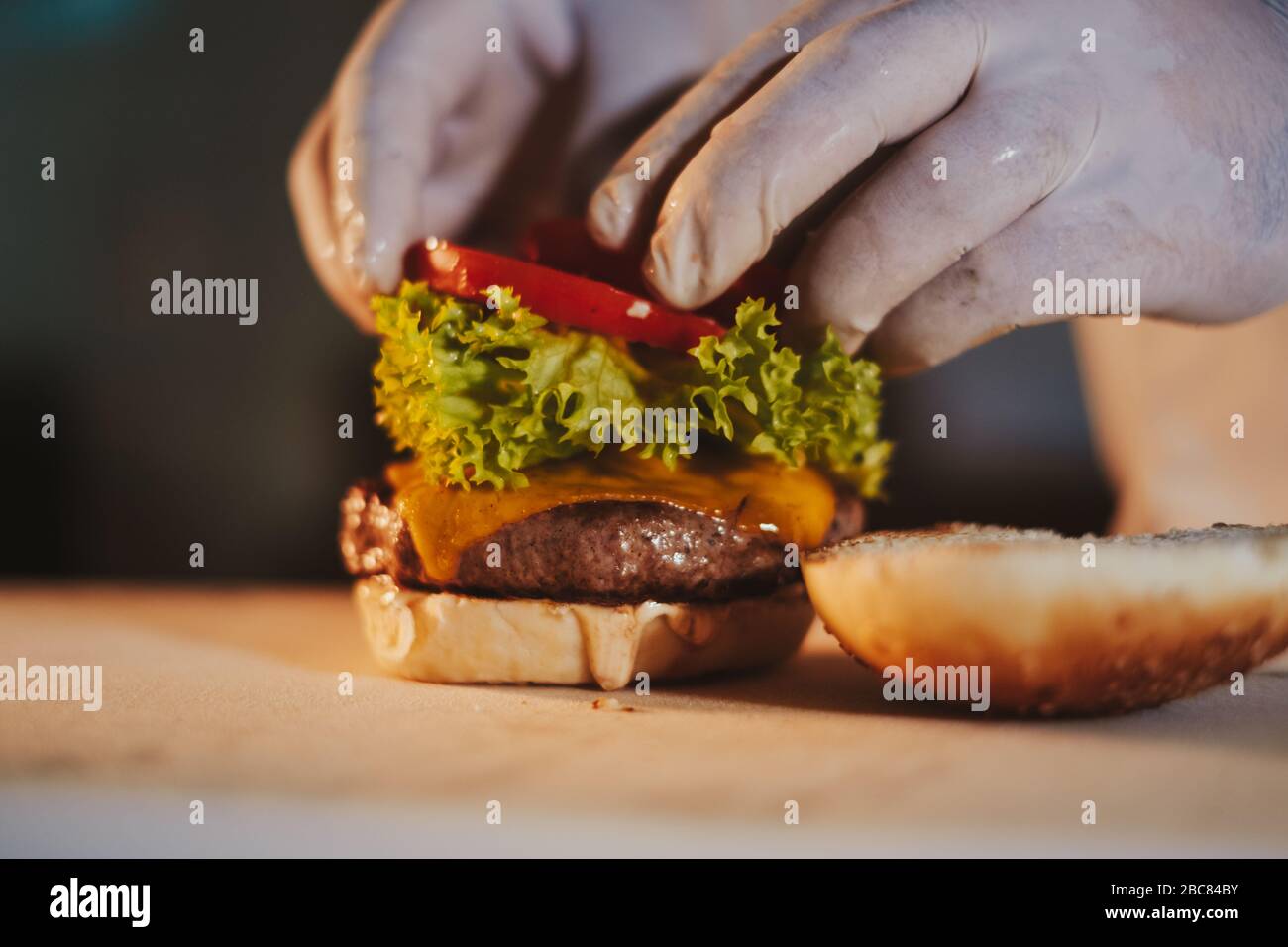 Küchenchefs stellen Cheeseburger zusammen, indem sie Tomaten mit Handschuhen hinzufügen Stockfoto