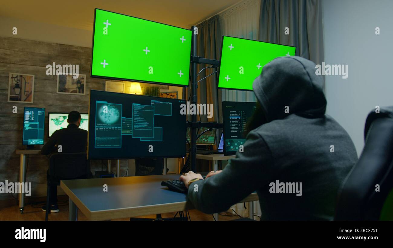Hacker mit einem Hoodies, der eine gefährliche Malware auf einem Computer mit grünem Bildschirm macht. Stockfoto