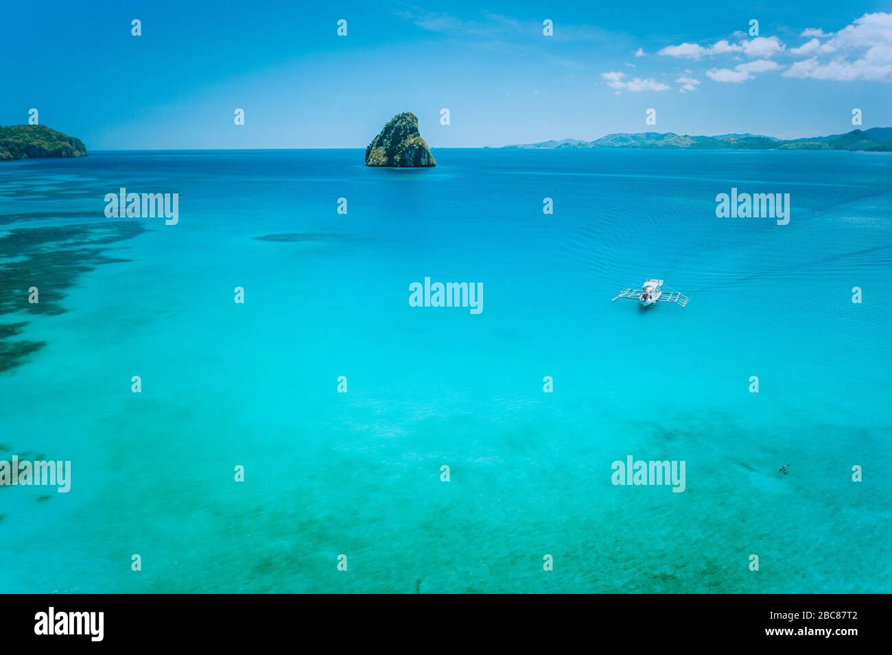 Ruhiger türkisfarbener Meeresoberfläche mit felsiger Insel und weißem, einheimischen banca-boot. El Nido Marine Reserve Park. Stockfoto