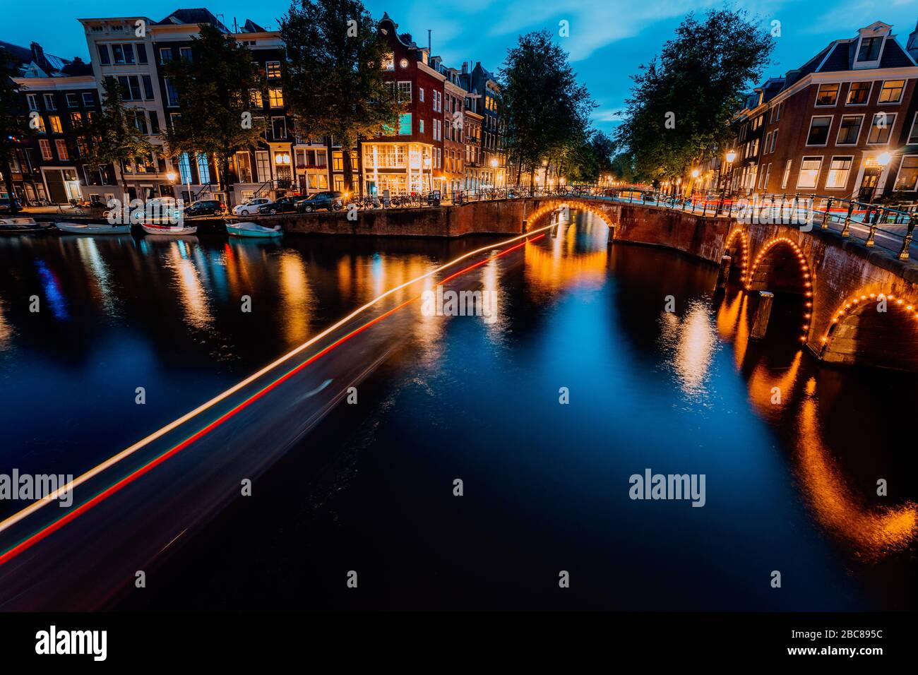 Amsterdamer Abend beleuchtete die Stadt. Touristische Bootslichtwege und Brückenreflexionen an den Kanälen Leidsegracht und Keizersgracht. Lang, z. B. Stockfoto