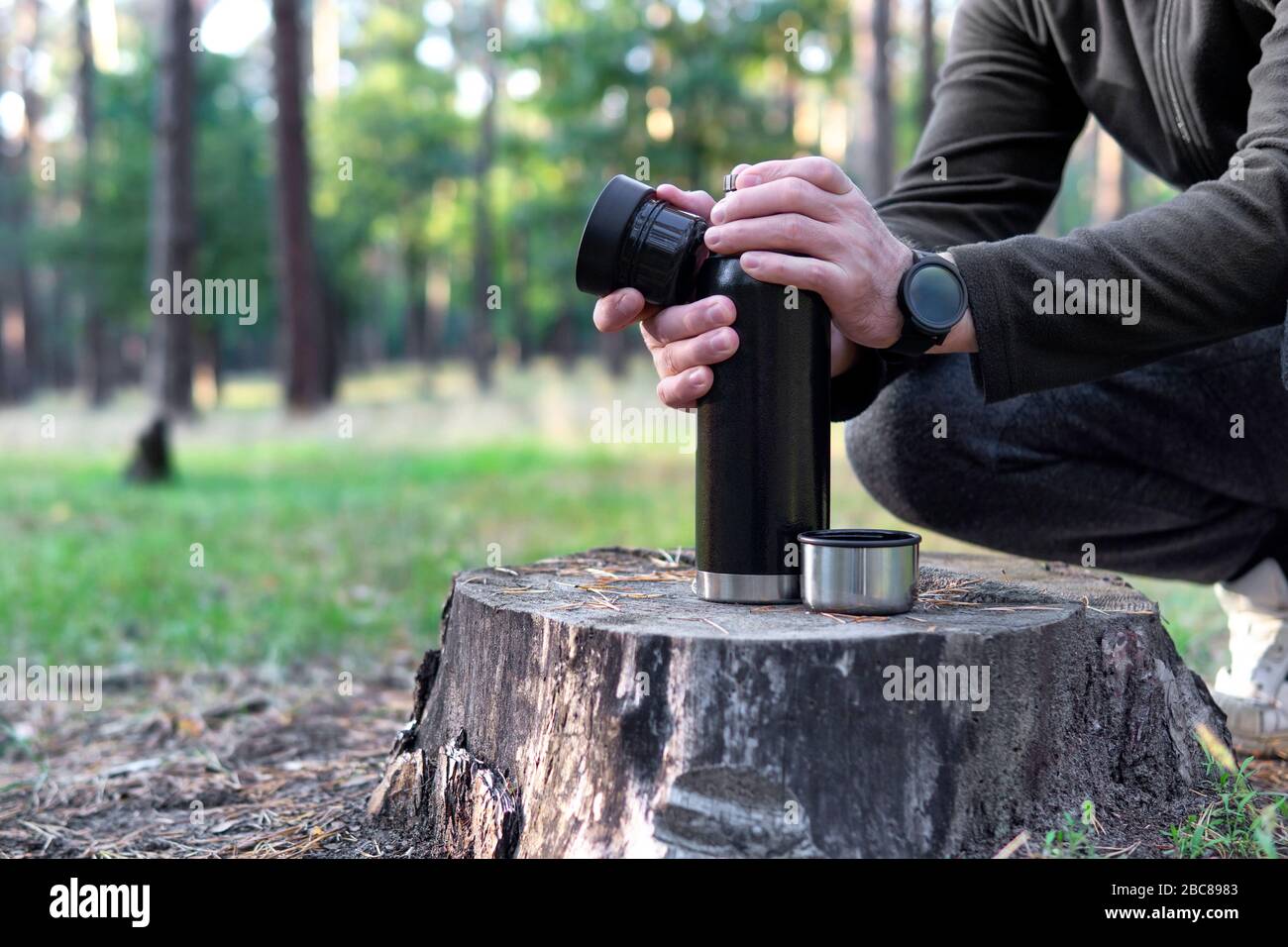 Man öffnet Thermosflasche, um ein Picknick auf einem Baumstumpf zu machen. Kaffeepause bei einem Spaziergang im Herbstpark Stockfoto