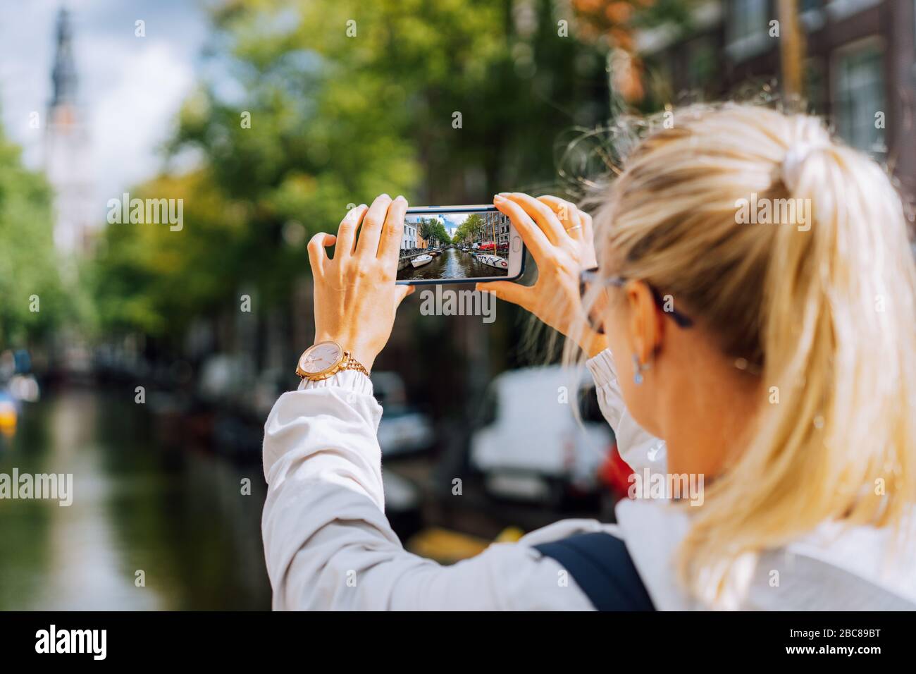 Frau Tourist, der ein Bild von Canal in Amsterdam auf dem Mobiltelefon. Warme gold Nachmittag Sonne. Reisen in Europa. Stockfoto
