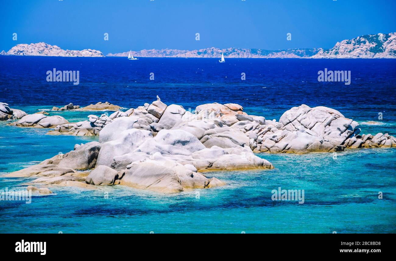 Granitfelsen im Meer, erstaunliche azurblaues Wasser, weiße Segelboote im Hintergrund in der Nähe von Porto Pollo, Sardinien, Italien. Stockfoto