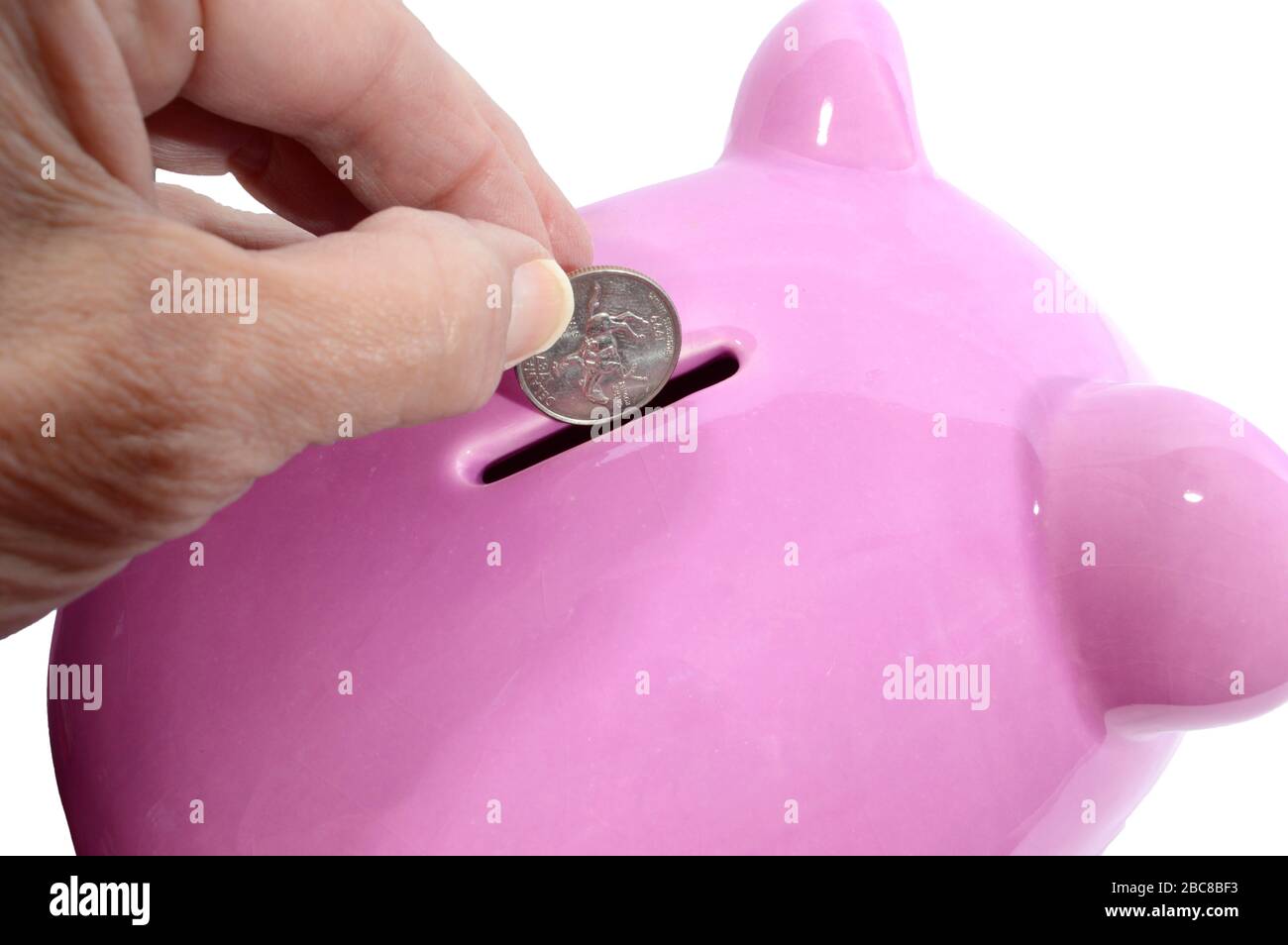 Horizontaler Nahschuss der Hand einer Frau, die ein Viertel in den Schlitz einer pinkfarbenen Schweinebank fällt. Weißer Hintergrund. Stockfoto