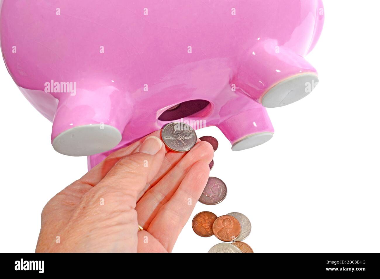 Horizontaler Nahschuss der Hand einer Frau, der Münzen aus dem Loch auf der Unterseite einer rosafarbenen Huckeparke zieht. Weißer Hintergrund. Stockfoto