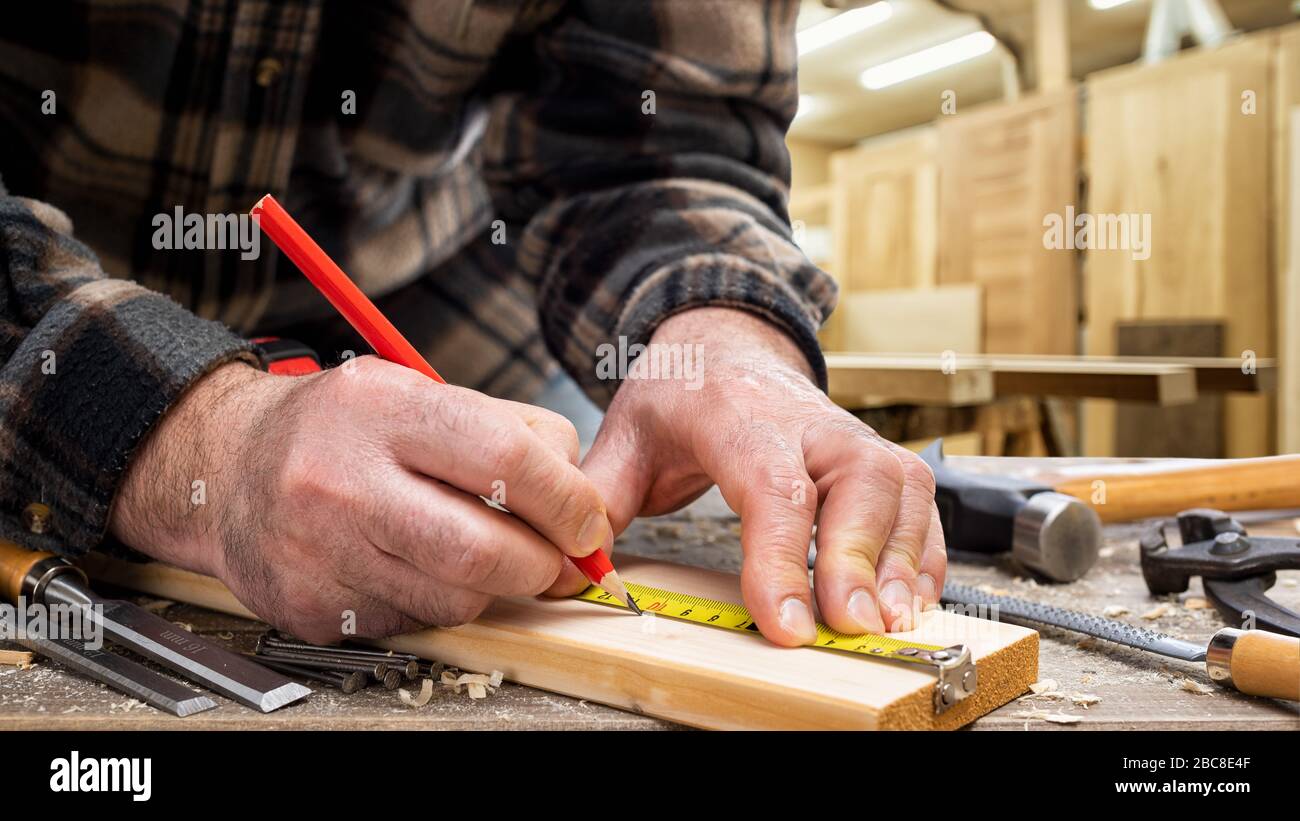 Nahaufnahme. Tischler mit Bleistift und Messgerät markiert die Messung auf einem Holzbrett. Bauindustrie, Zimmerei. Stockfoto