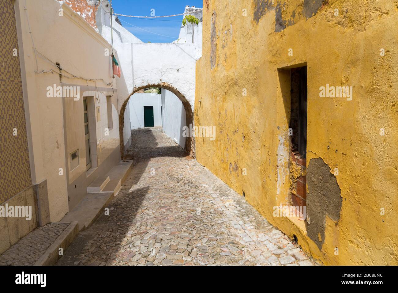 Enge Straße mit glatten abgenutzten Steinen und Bogen mit bemalter Wand, Loule, Algarve, Portugal Stockfoto