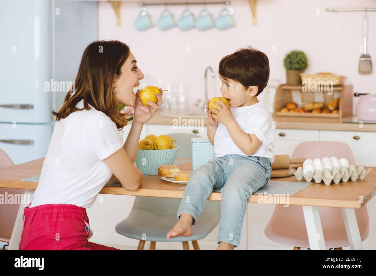 Mutter und kleiner Sohn essen frische gelbe Birnen in der Küche. Stockfoto