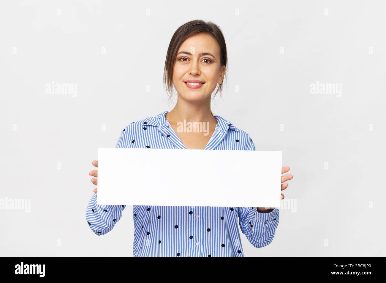 Fröhliche brünette Frau in elegantem blauem Hemd mit weißem Banner, isoliert auf Weiß Stockfoto