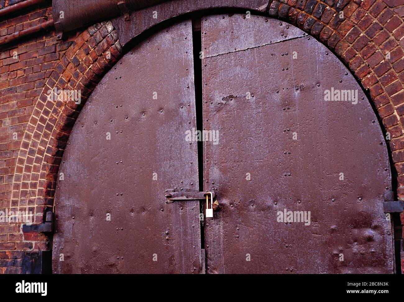 Architektur. Eisenbahnbogen aus viktorianischem Backstein. Rostige, mit einem Vorhängeschloss verschlossene Tür. Stockfoto