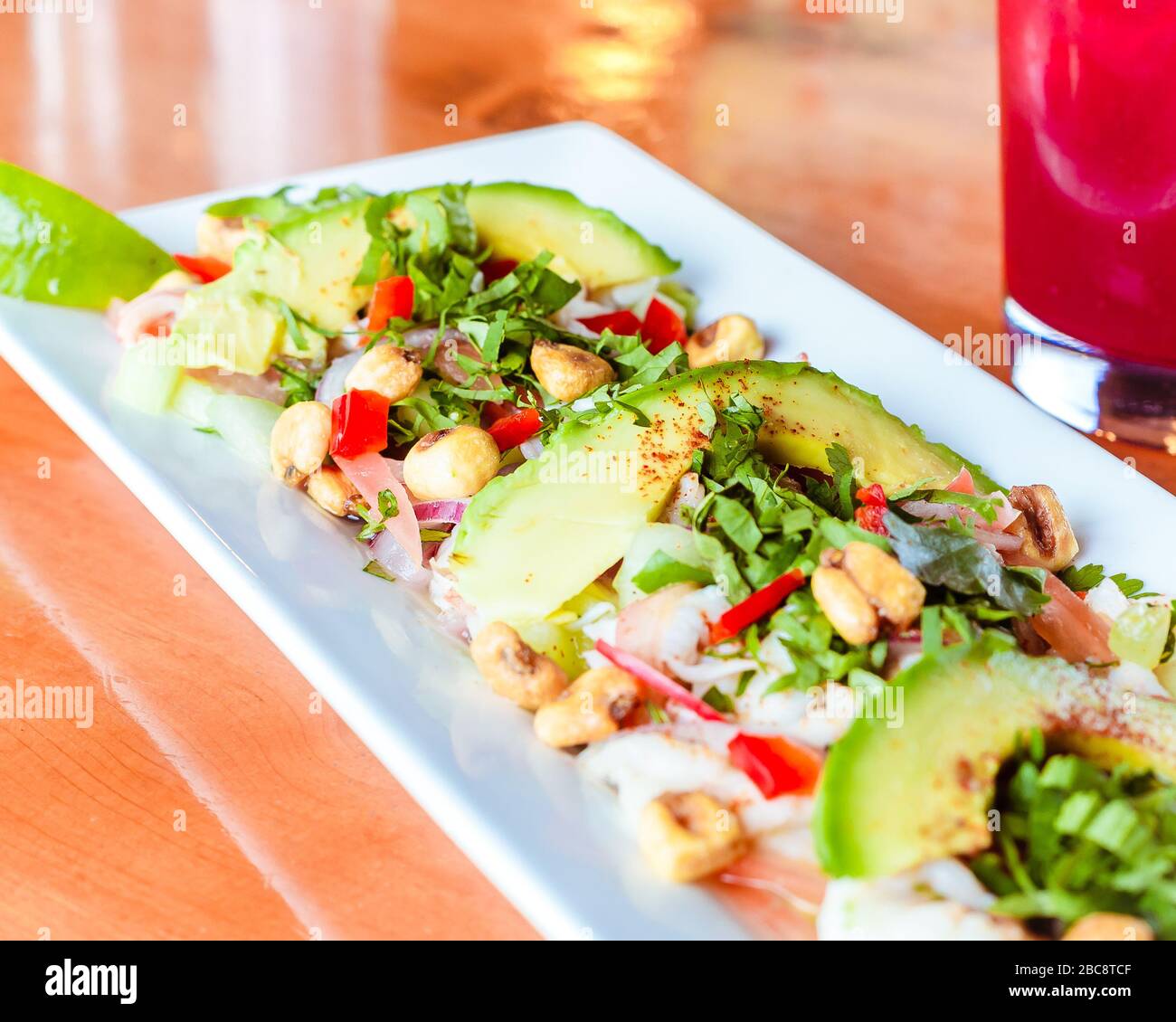 Traditionelle mexikanische Avocado Ceviche Platte auf hell glänzenden Holzoberfläche in mexikanischem Restaurant mit traditionellem mexikanischen Hibiskus Getränk Stockfoto
