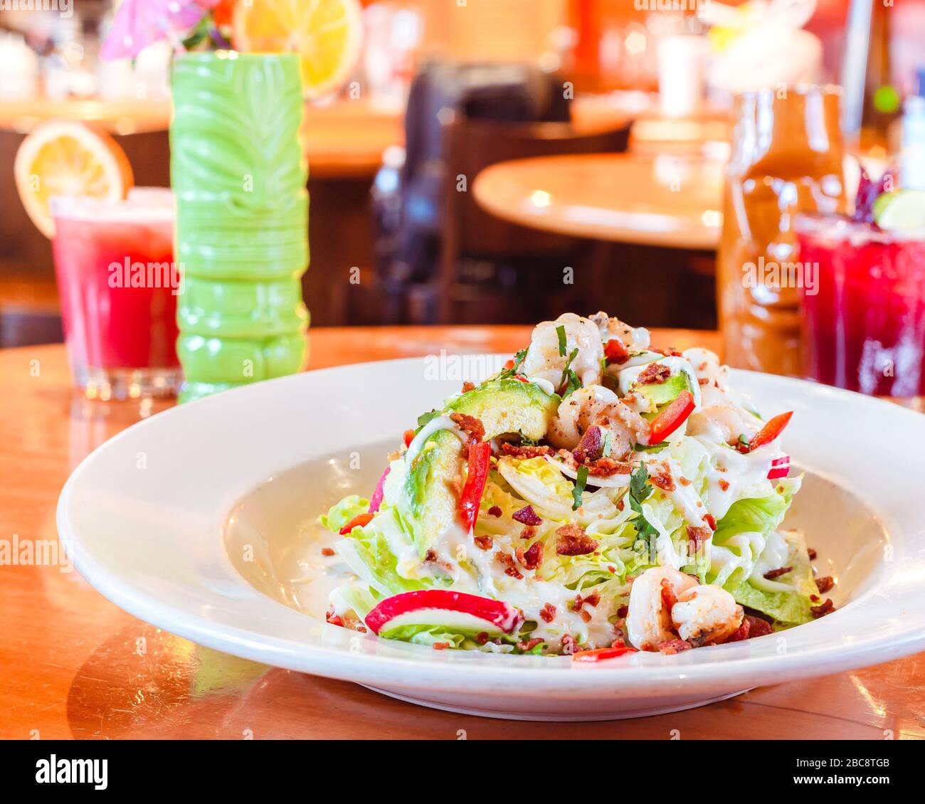Schmackhafter traditioneller mexikanischer Salat mit Dressing und rotem Pfeffer auf einer hellbraunen Holzoberfläche in einem traditionellen mexikanischen Restaurant, das von tra umgeben ist Stockfoto