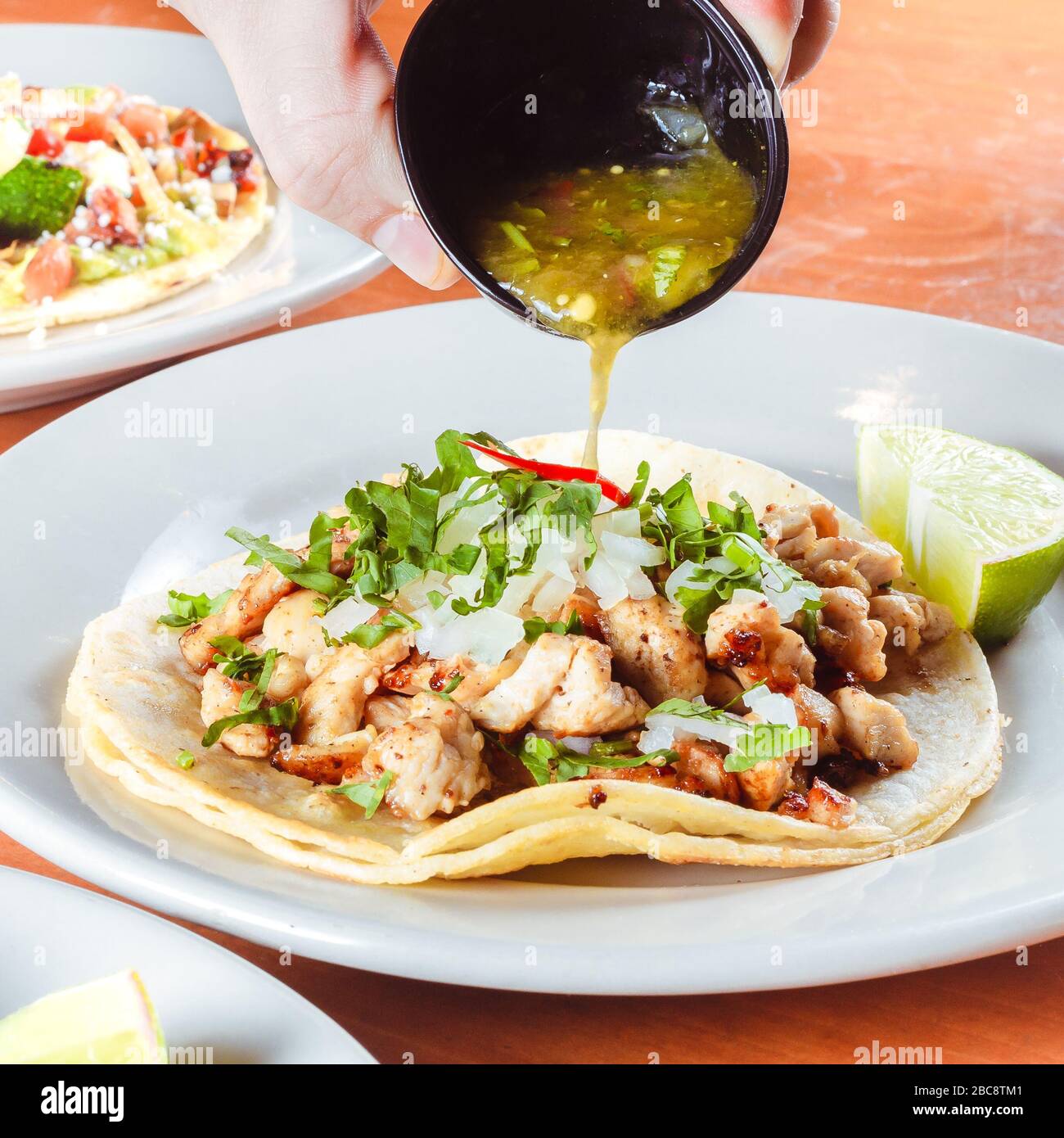 Taco Platte mit Mann gießen grünen Salsa in einem traditionellen mexikanischen Restaurant umgeben von anderen traditionellen mexikanischen Platten Getränke und andere Restaurants Stockfoto