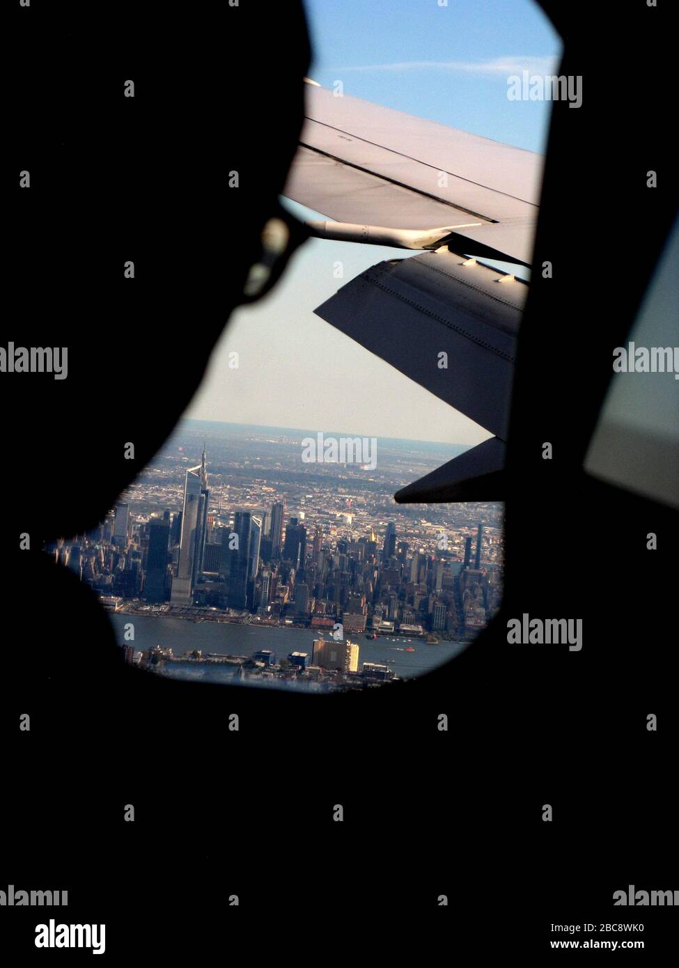 Silhouette eines Mannes in einer Brille, der von einem Flugzeugfenster aus auf die Skyline von Manhattan blickt Stockfoto