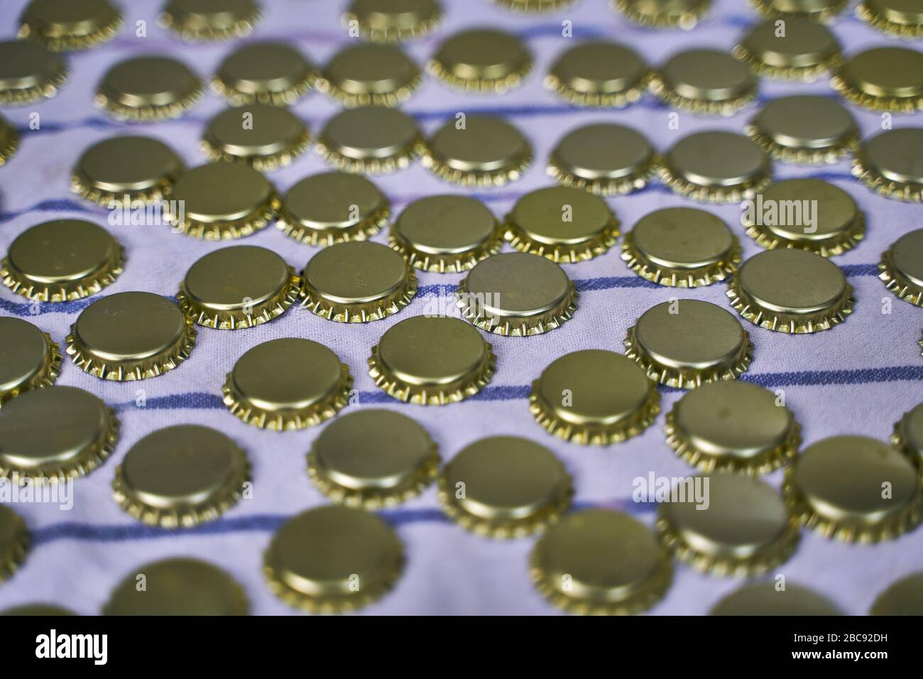 Metall- und Goldbierkappen in Reihe auf einem weißen und blauen Tuch in einer Brauerei Stockfoto