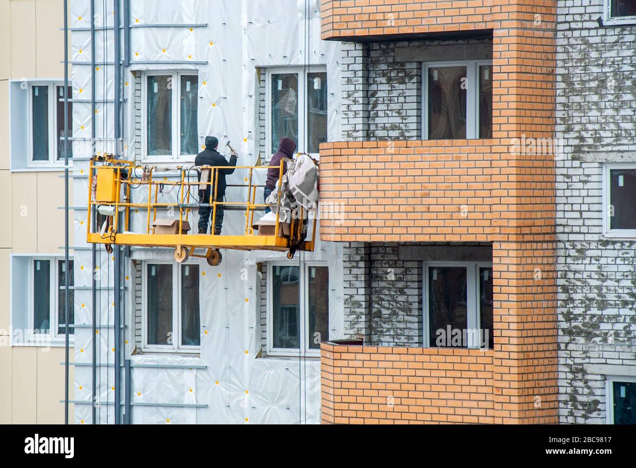 Die Wände des Gebäudes sind isoliert und eingeebnet. Industriearbeitsbereich. Arbeiter installieren eine vorgefertigte Glasscheibe auf einer Baustelle. Faci Stockfoto