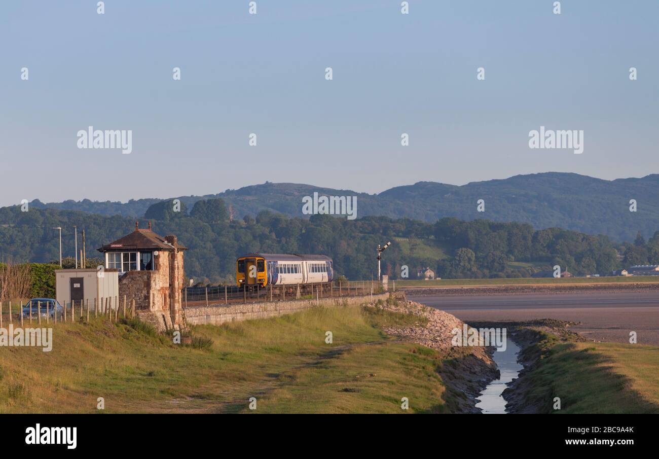 Sprinterzug der Northern Rail Klasse 156, der mit einem leeren Bestandszug am frühen Morgen an der Eisenbahnlinie der Cumbrian Coast vorbei an der Arnside Signalbox fährt Stockfoto