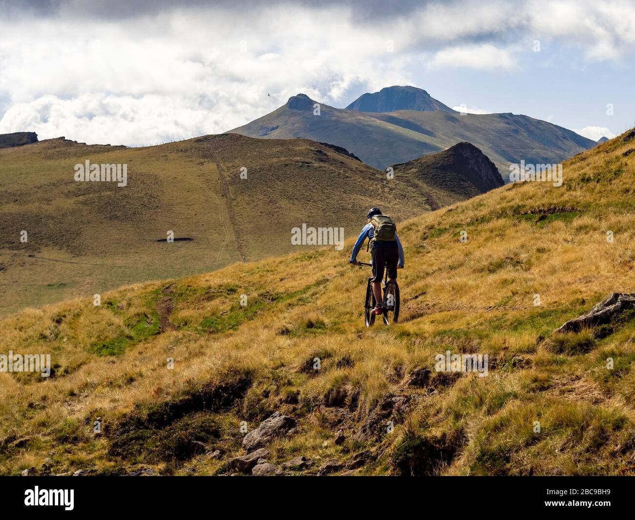 Mountainbikers auf dem Einzelweg GR 400 auf einem schmalen Bergwanderweg über hohe Wiesen bei Le Pas Rouge, mit Suc de la Blatte, Puy de la to Stockfoto