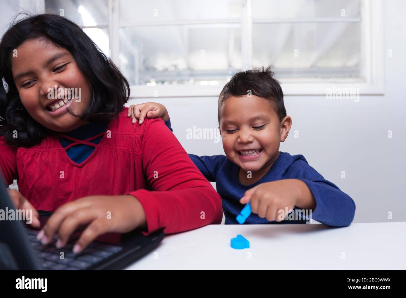 Junge Geschwister sitzen zu Hause vor einem Laptop während des Fernunterrichts-Klassenzimmers zusammen. Stockfoto