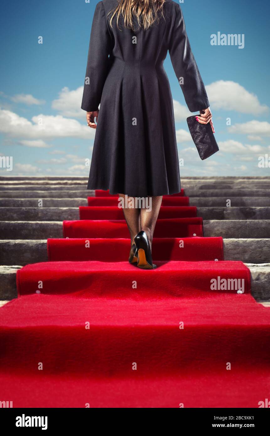 Elegante Frau in schwarzem Mantel klettert auf einem roten Teppich Treppe Stockfoto