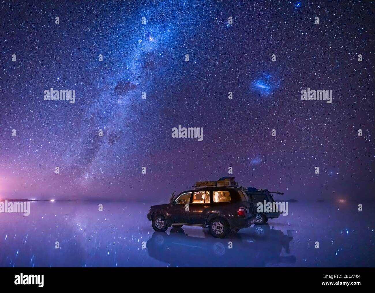 Sternenhimmel mit Milchstraße über Salzwohnung von Uyuni, Bolivien. Zwei auf dem Feld geparkte Jeeps reflektieren die Sterne im Wasser. Stockfoto