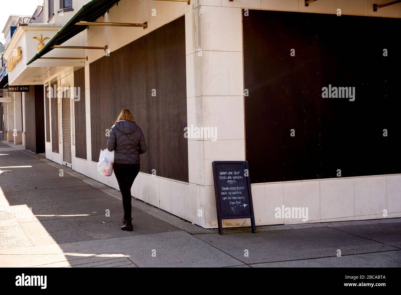 Vancouver, Kanada, 03. April 2020. Eine Frau läuft an Geschäften in der South Granville Street vorbei, die geentert wurden, um während der COVD-19-Pandemie Beutezüge zu verhindern. Stockfoto