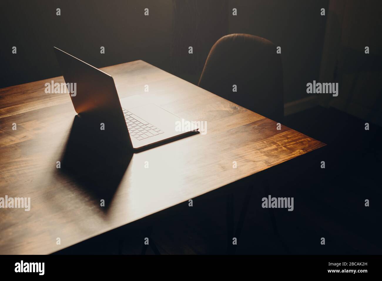 Ein Laptop auf einem Holztisch in einem dunklen Bereich mit Lederstuhl. Draufsicht. Stockfoto