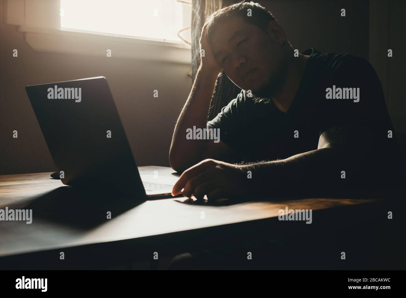 Ein Asiat arbeitet auf Laptop in dunklen Bereich. Geste der Traurigkeit. Stockfoto