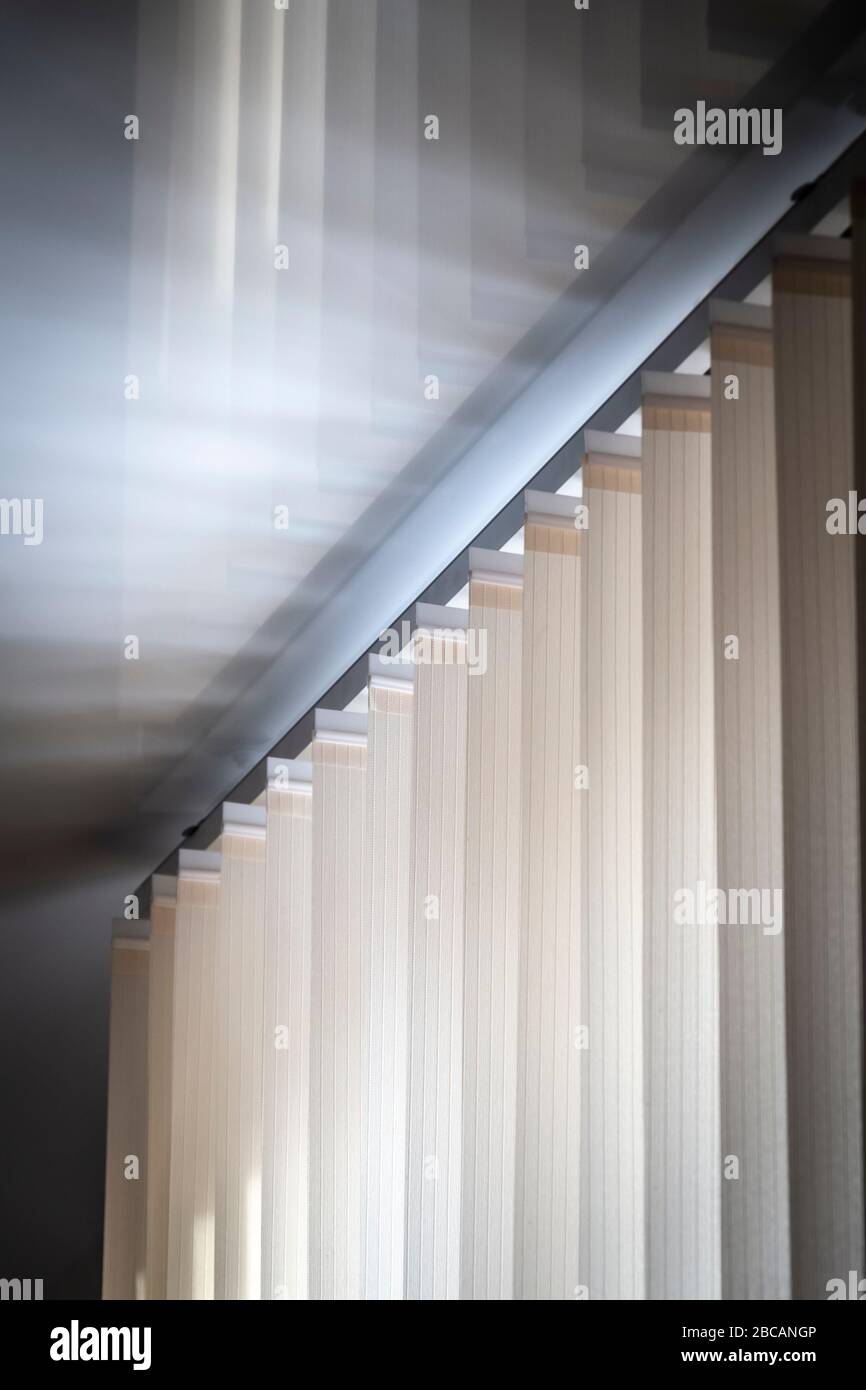 Teil des Mechanismus von beigefarbenen vertikalen Jalousien auf dem Hintergrund einer Spiegel-Stretchdecke. Stockfoto