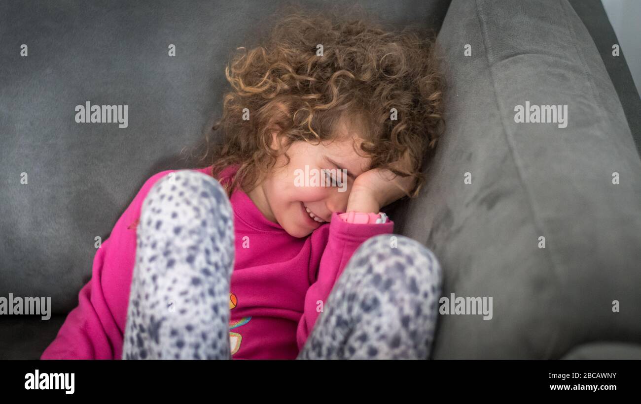 Isoliertes Nahporträt eines 7-jährigen Mädchens, das im Sofa im Zimmer sitzt und lächelt Stockfoto