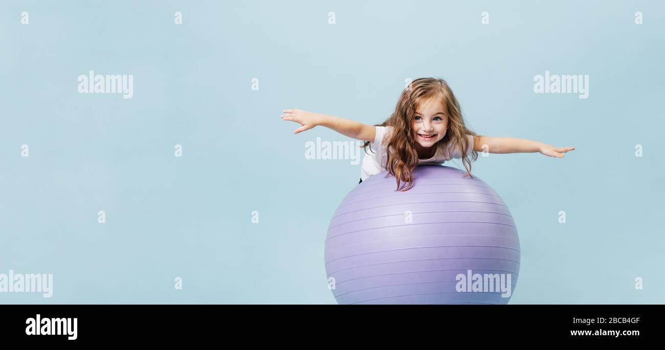 Lockig-haarige lustige Mädchen spielen auf einem gymnastischen Ball Stockfoto