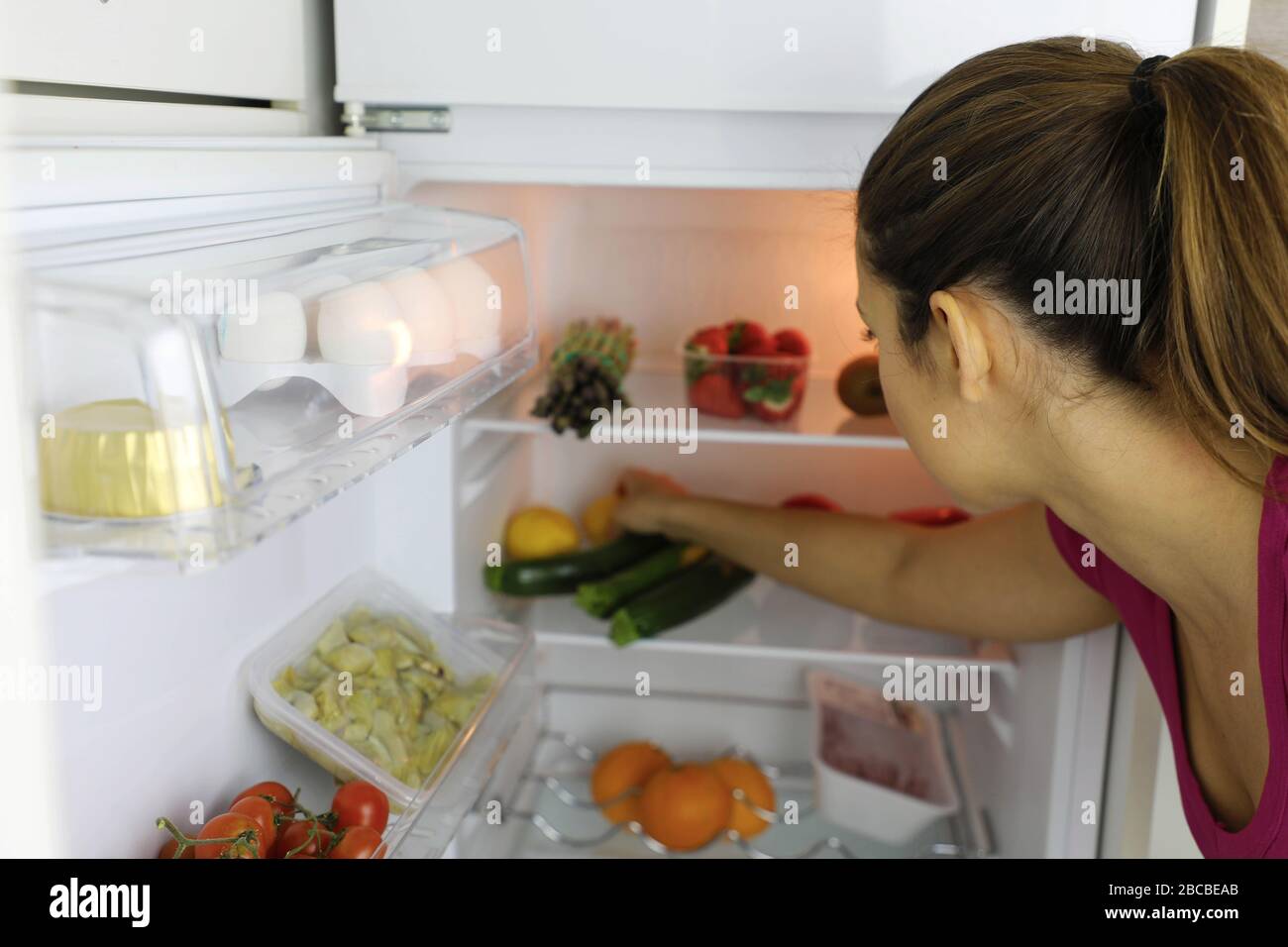 Rückansicht der jungen Frau auf der Suche nach gesunden Lebensmitteln im Kühlschrank Stockfoto