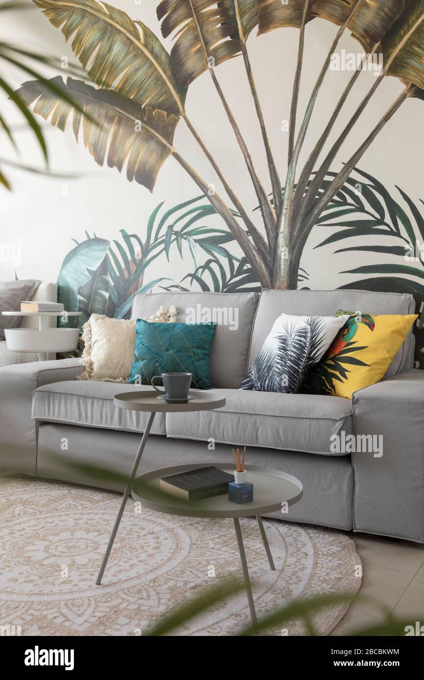 Kleines graues Sofa vor floraler Tapete. Stockfoto