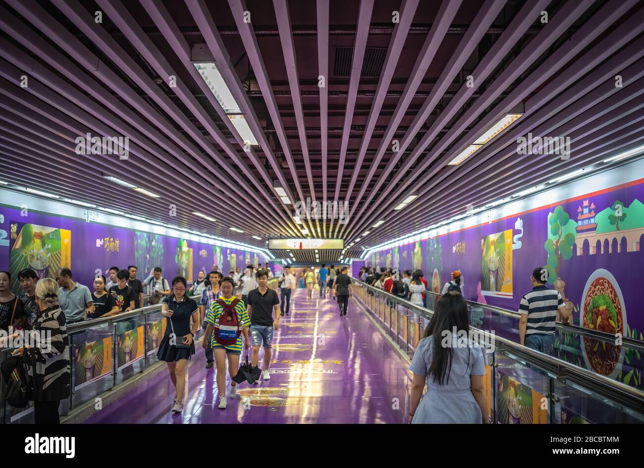 Chongqing, China - August 2019: Pendler, die im farbenfrohen, bemalten U-Bahn-Tunnel zu Fuß unterwegs sind, führen zu U-Bahn-Zügen Stockfoto