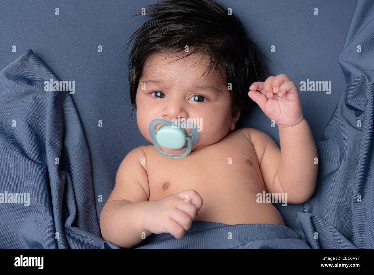 Baby Saugen Schnuller, Kleinkind Junge Saugen Schnuller, Kind liegt auf dem Rücken isoliert über blauen Hintergrund Stockfoto