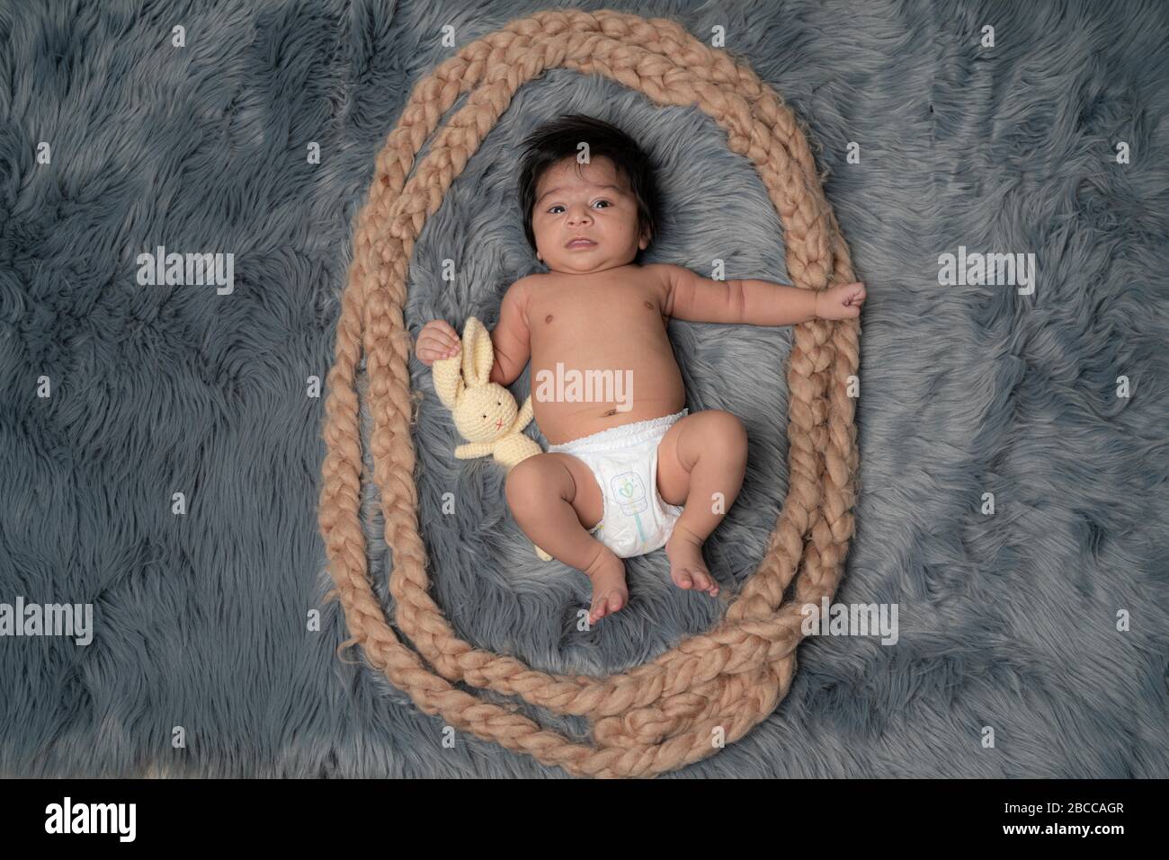 Porträt eines neugeborenen Jungen, Alter 1 Monat, in einer Windel, schwarzes Haar, blaue Augen auf grauen Pelzdecke mit einem Teddybären und lächelnd. Familie, Liebe, ch Stockfoto