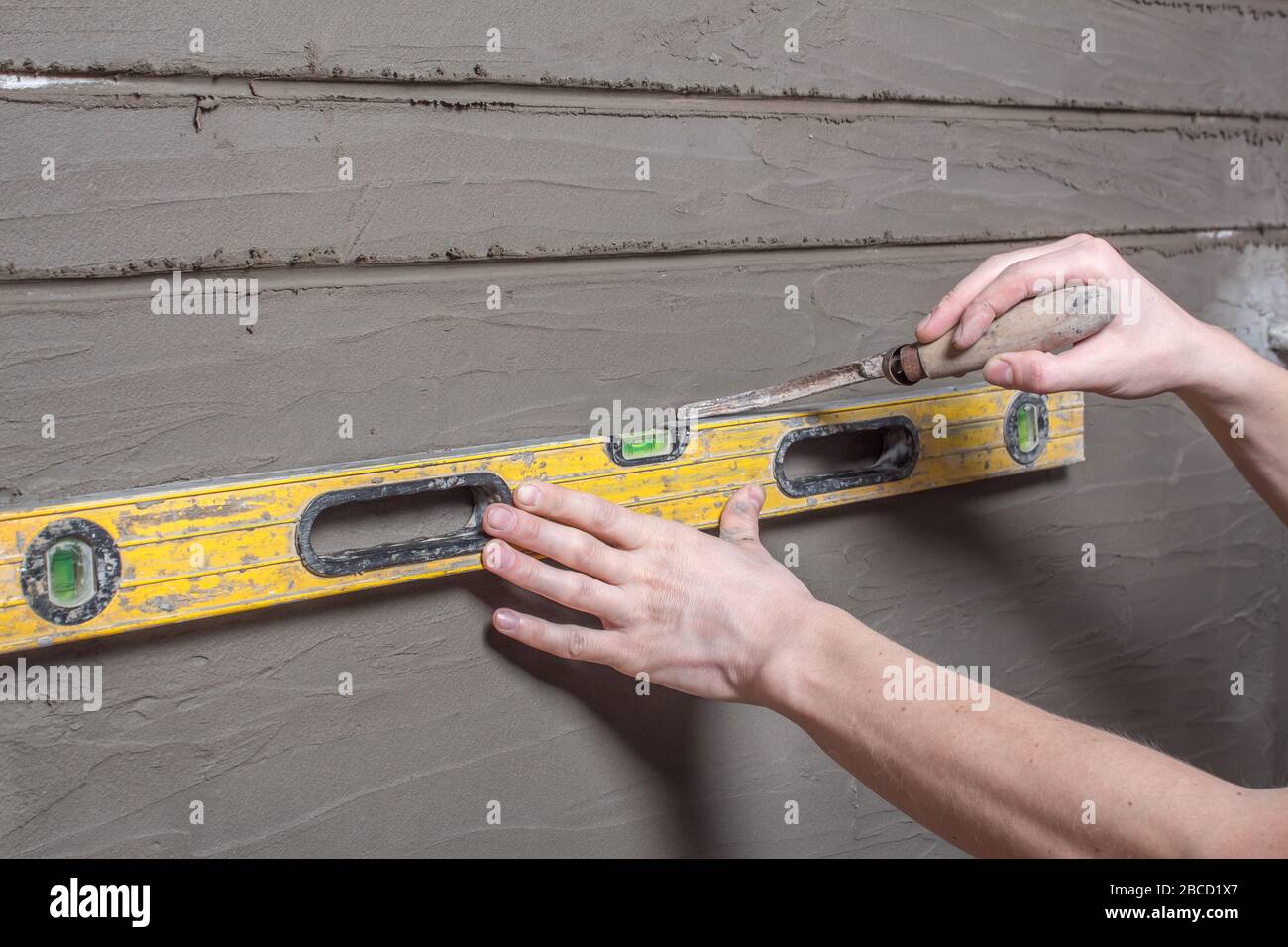 Die Hand zieht horizontale Streifen mit Stickerei auf den Putz. Der Erbauer behält die Bauhöhe und markiert die Wand. Reparatur der Wände im ho Stockfoto