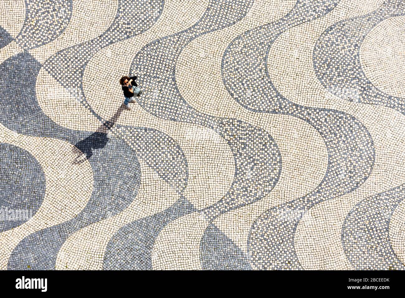 Blick auf einen Touristen, der durch die wellenartig gemusterte Pflasterung unter dem Padrão dos Descobrimentos in Lissabon spazieren geht Stockfoto