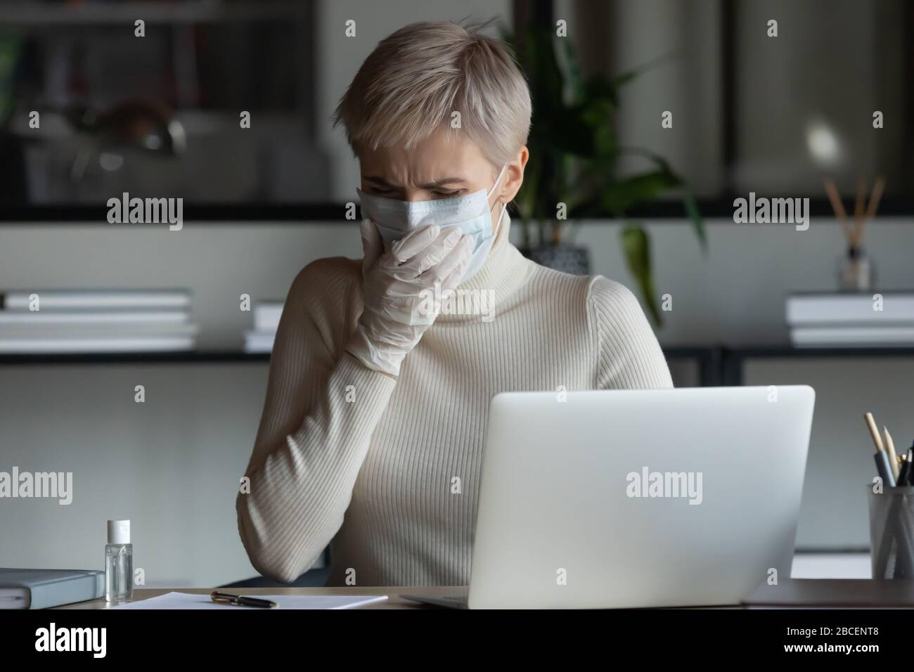 Betonte junge Geschäftsfrau in der medizinischen Maske und Schutzhandschuhe hustend. Stockfoto