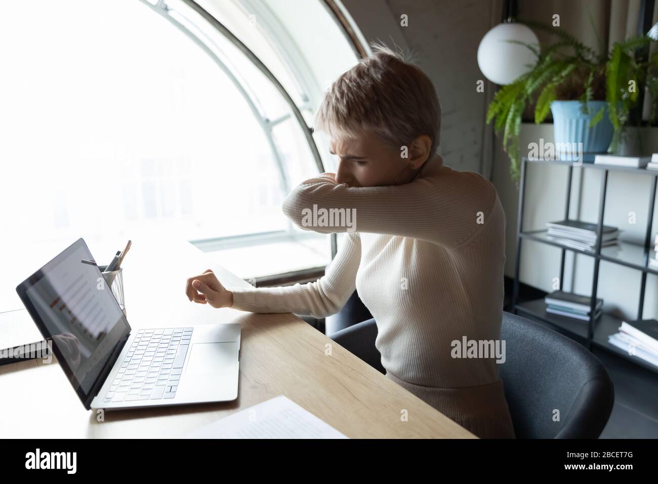 Junge Angestellte des weiblichen Unternehmens hustet Niesen im Ellenbogen. Stockfoto