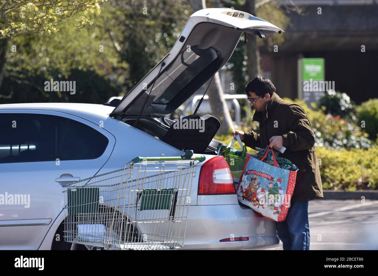 Ein Mann, der Lebensmittel in den Kofferraum seines Autos in einem Supermarkt-Parkplatz in Großbritannien legt Stockfoto